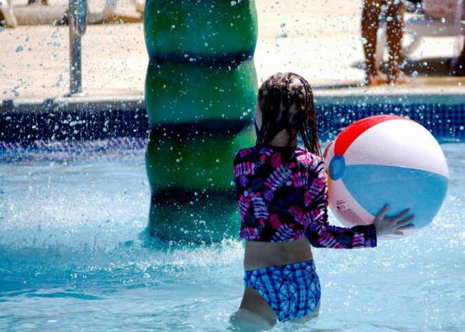 a little girl playing with a beach ball in a pool