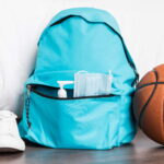 Sac à dos de sport bleu turquoise posé au sol à côté d'un ballon de basket et d'une paire de baskets blanches