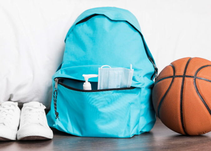 Sac à dos de sport bleu turquoise posé au sol à côté d'un ballon de basket et d'une paire de baskets blanches